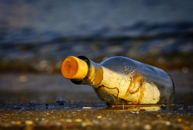 A paper message wrapped with string in a bottle sealed with a cork lies washed up on shore resting on wet sand. It's been through a lot to get here.